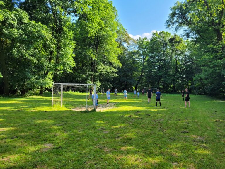Grupa wychowanków z gośćmi na boisku rozgrywa mecz piłki nożnej z okazji Dnia Dziecka.