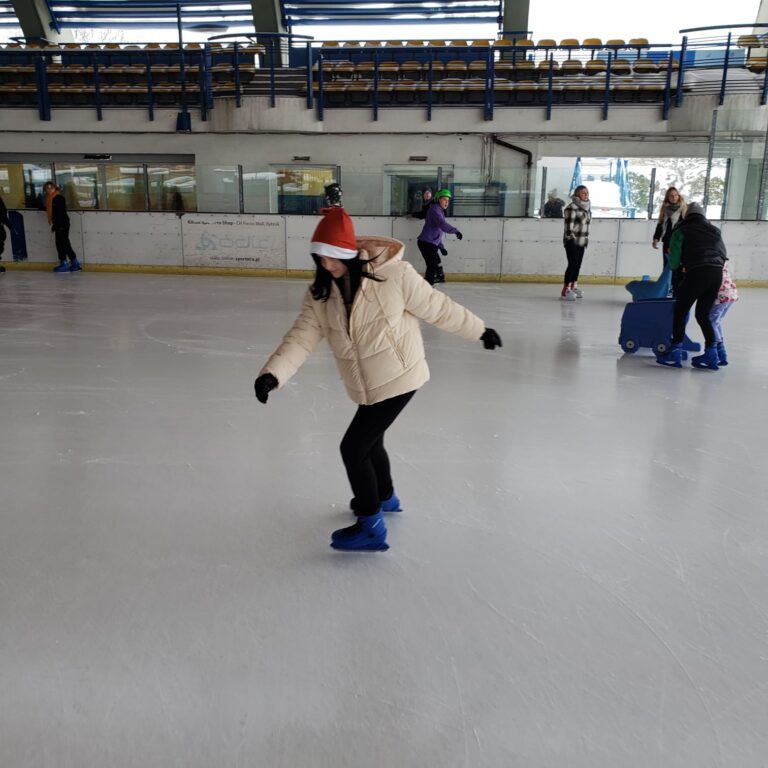 Dziewczyna w czapce mikołaja jeżdzi na łyżwach na lodowisku.